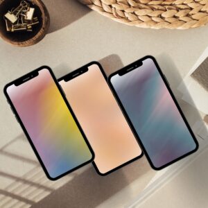 Three iPhone mockups displaying nice iPhone wallpapers with soft gradient mobile wallpaper designs in pink, yellow and lavender tones, styled on a neutral flat lay background.